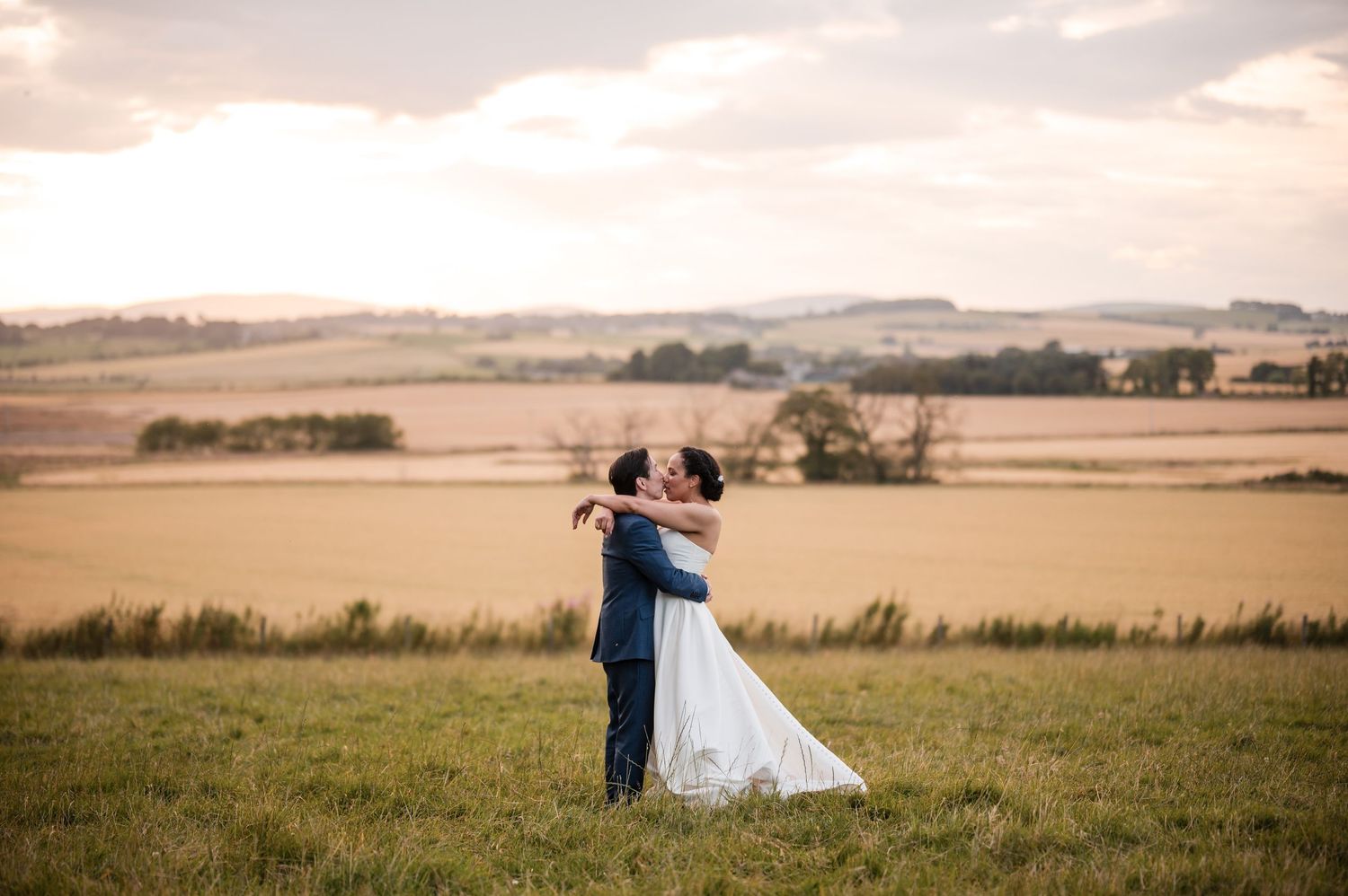 Couple walking through an open field during sunset with dramatic sky.