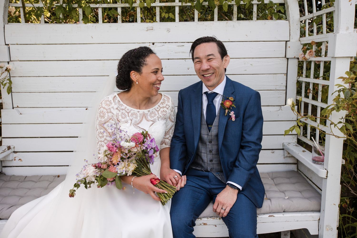 Couple sitting together on white porch with garden trellis background.