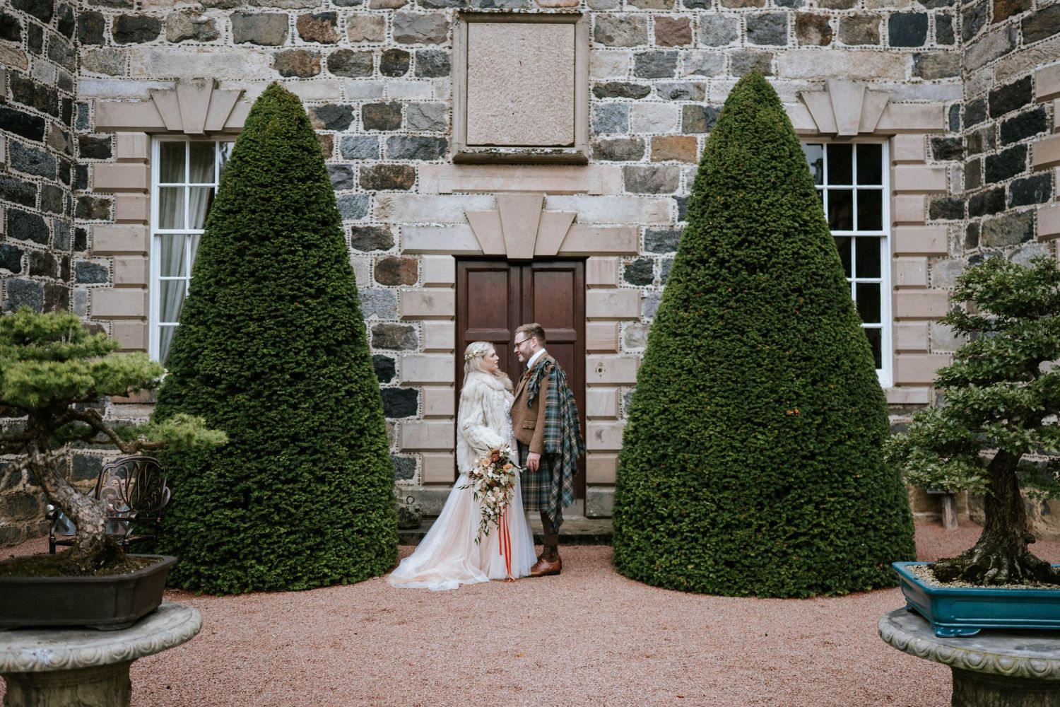 Elegant stone mansion with manicured topiary bushes serves as wedding venue backdrop.