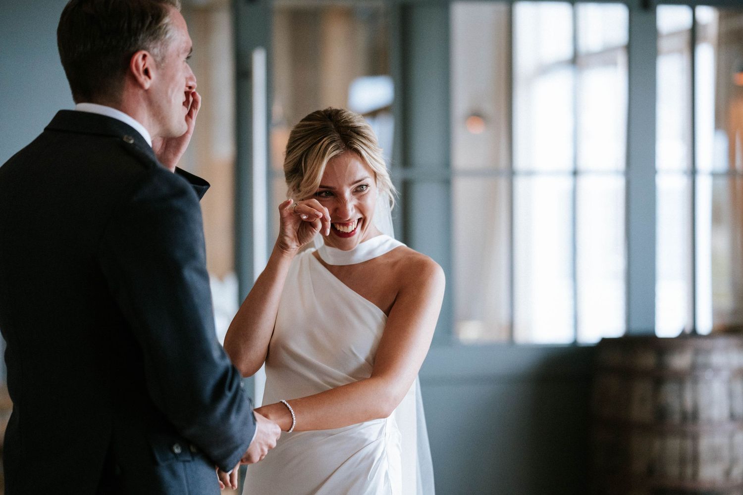 Wedding couple sharing an intimate moment in front of large windows in an elegant venue.