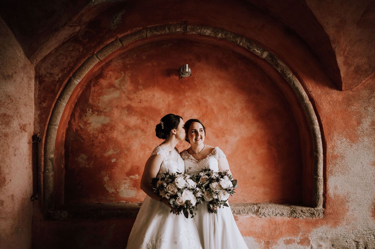 A romantic wedding photo against rustic terracotta arches with white floral bouquets. Meldrum House Wedding Photography.
