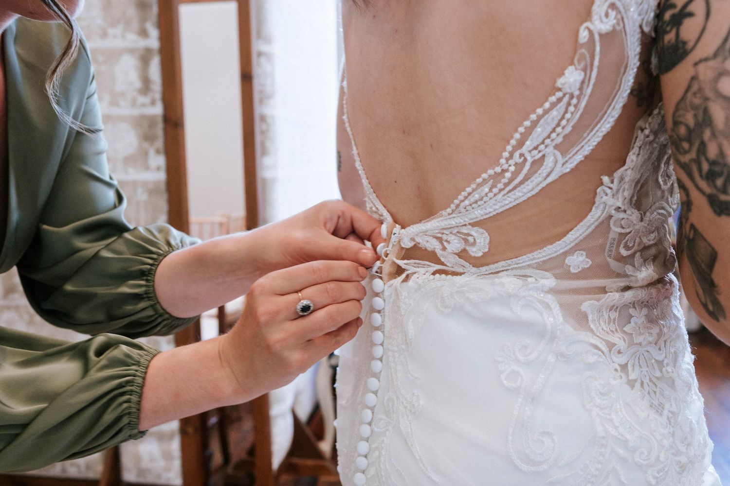 Close-up detail of delicate lace buttons being fastened on the back of a wedding dress.