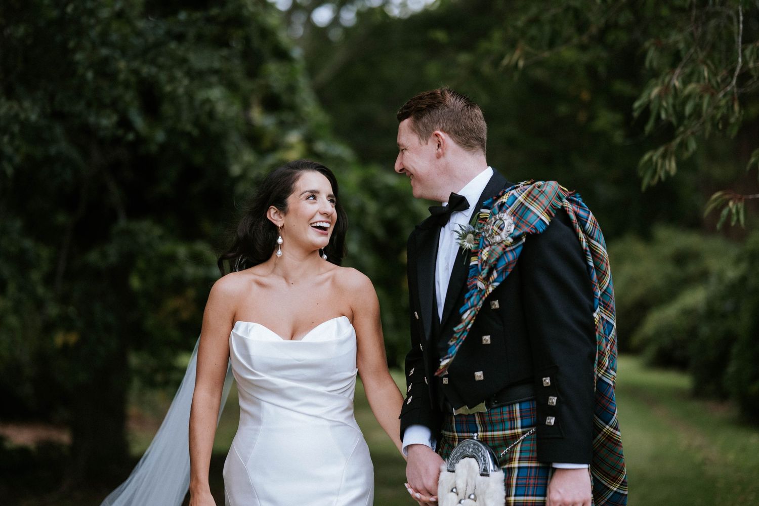 Candid wedding portrait showing joyful laughter between couple in white gown and Scottish formal wear.