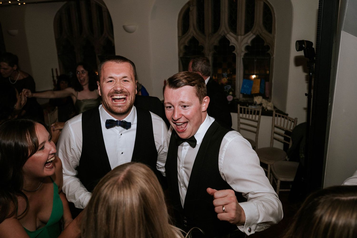 Joyful celebration with guests dancing and laughing at an indoor wedding reception.