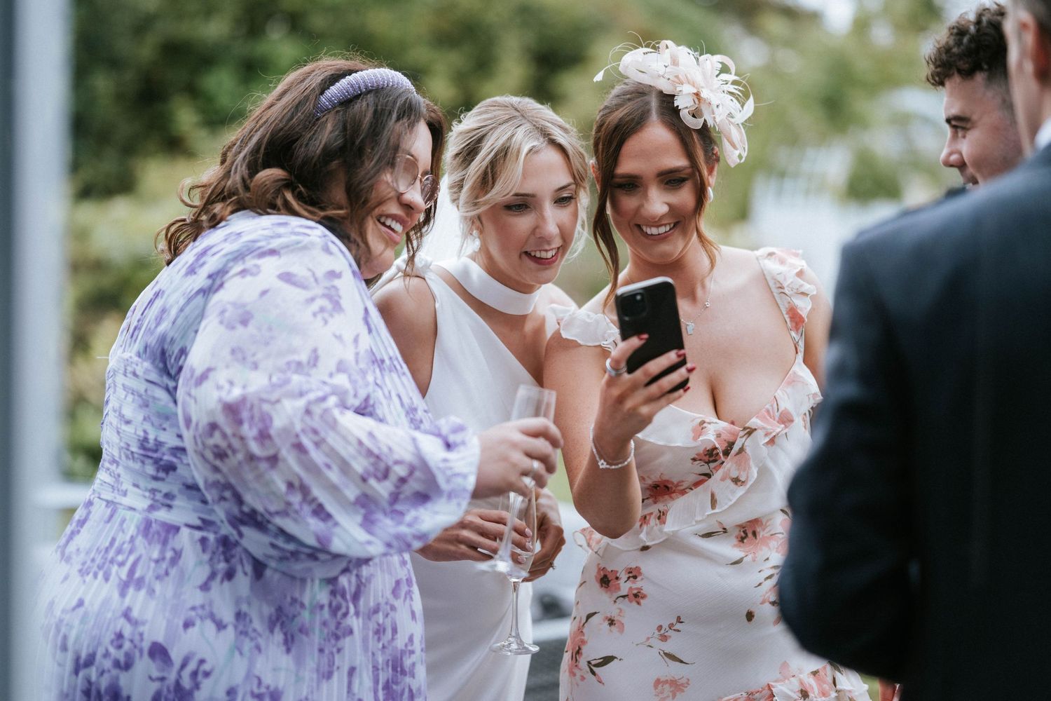 Wedding guests in floral dresses taking photos during outdoor celebration.
