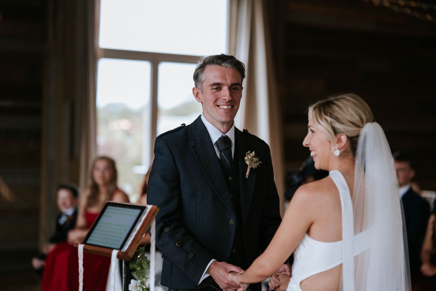 Wedding ceremony taking place in an elegant indoor venue with large windows.