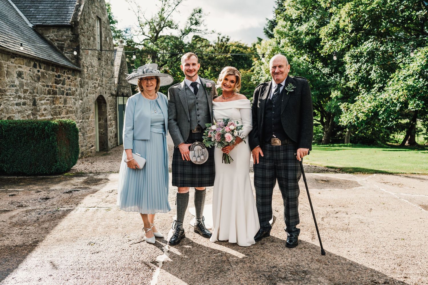 Wedding ceremony group gathers on stone path surrounded by lush green gardens.