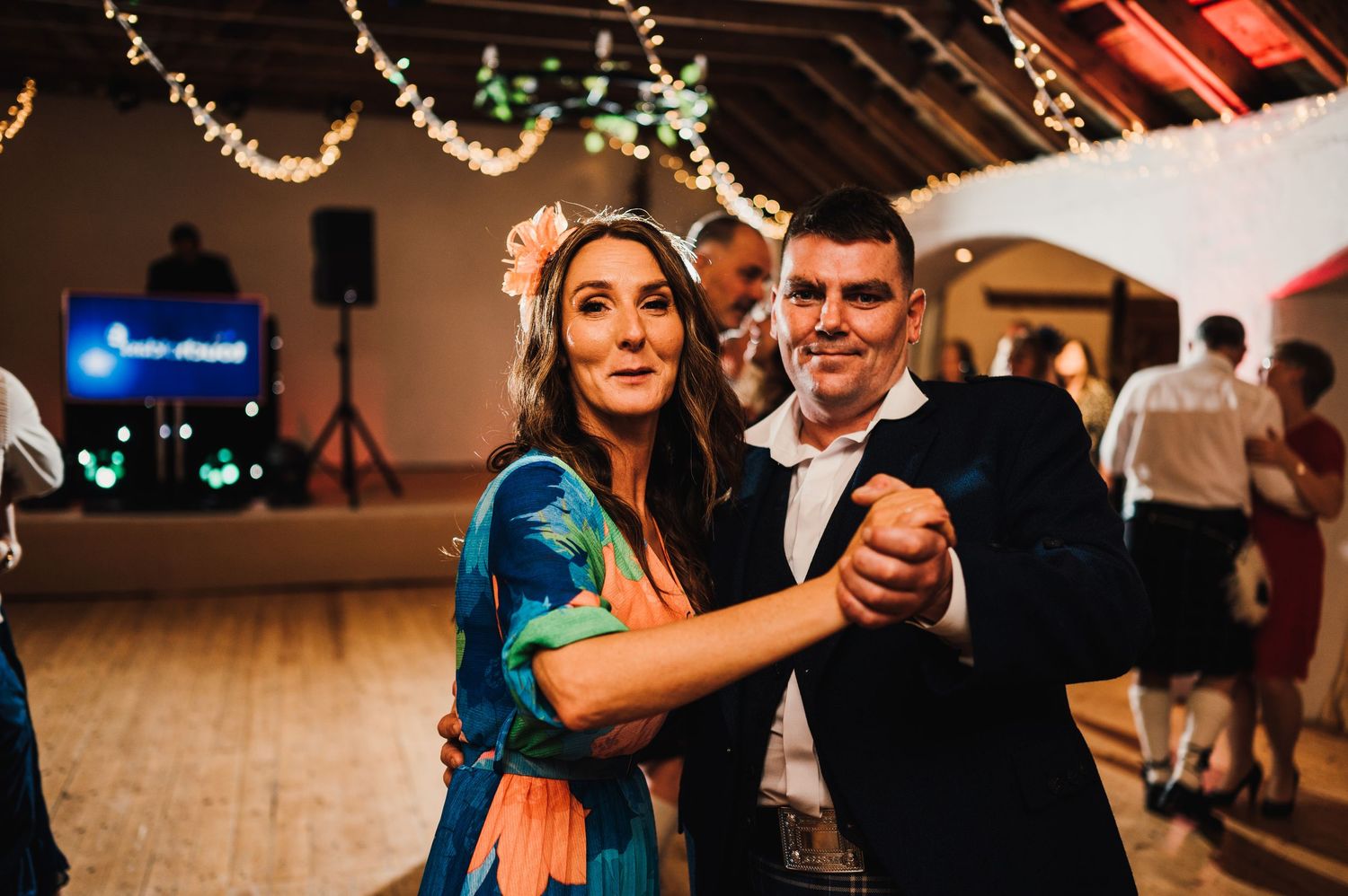 Couples dancing and enjoying themselves at a wedding reception with string lights overhead.