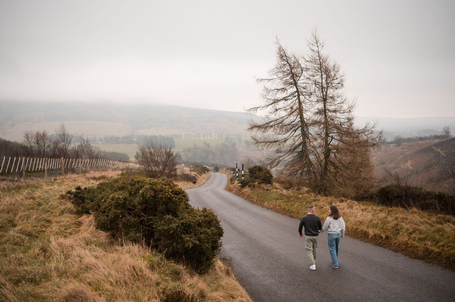 Engagement photography session Aberdeen. A winding road curves through foggy moorland hills.