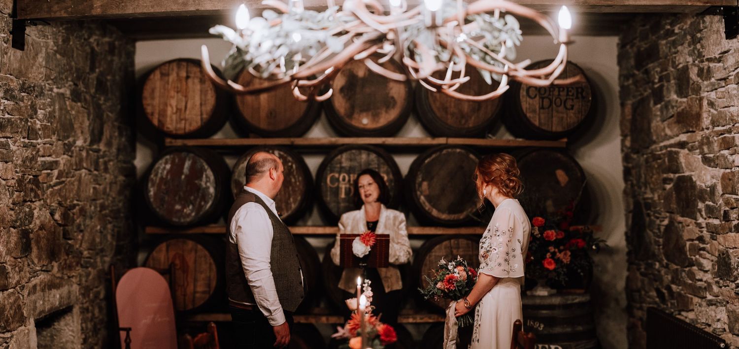 Wedding celebration in stone-walled wine cellar with elegant chandelier and barrel backdrop.