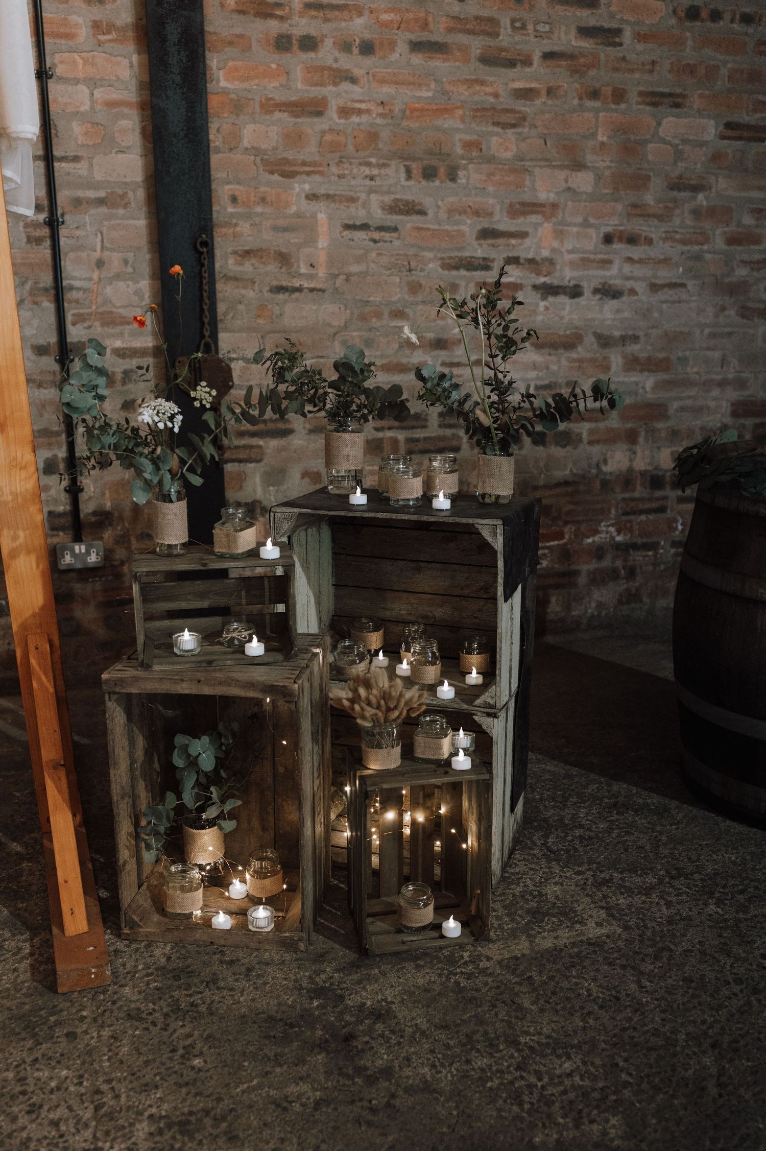 Vintage wooden crates with candles and floral arrangements create a romantic corner display against brick wall.
