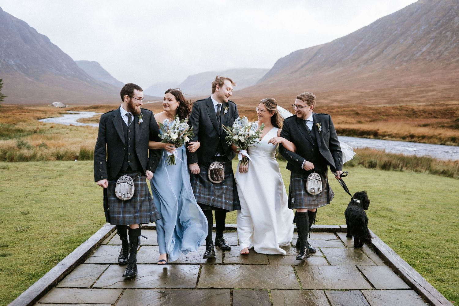 Group photo on wooden platform with scenic Scottish Highlands mountains in background.