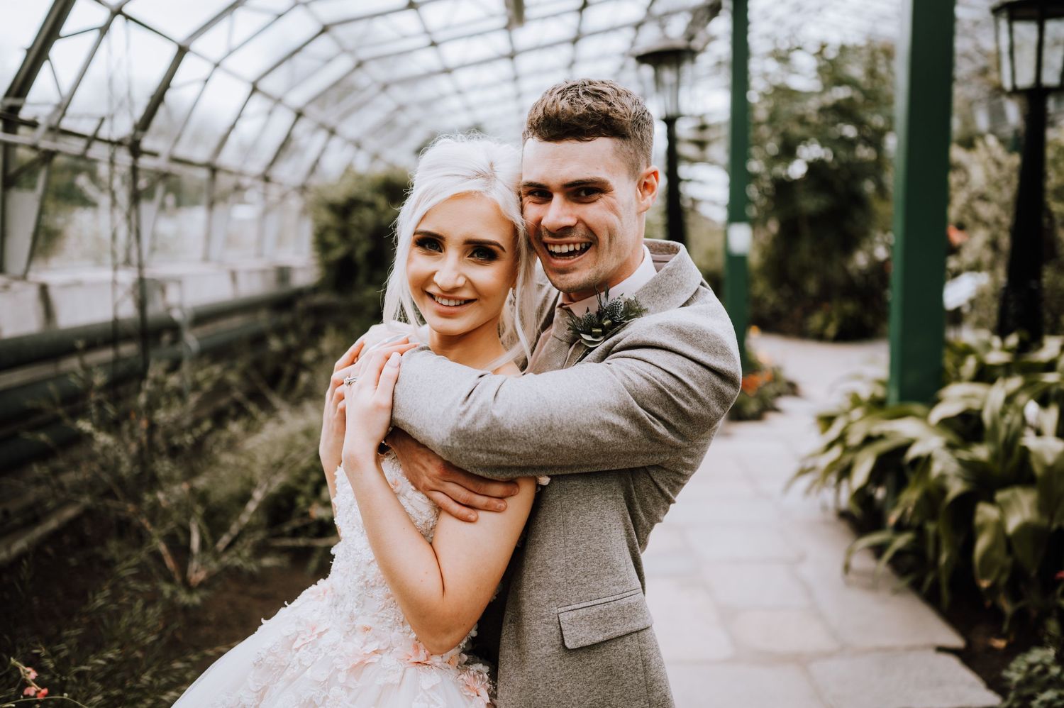 A romantic wedding photo of a couple embracing in a greenhouse with natural lighting.
