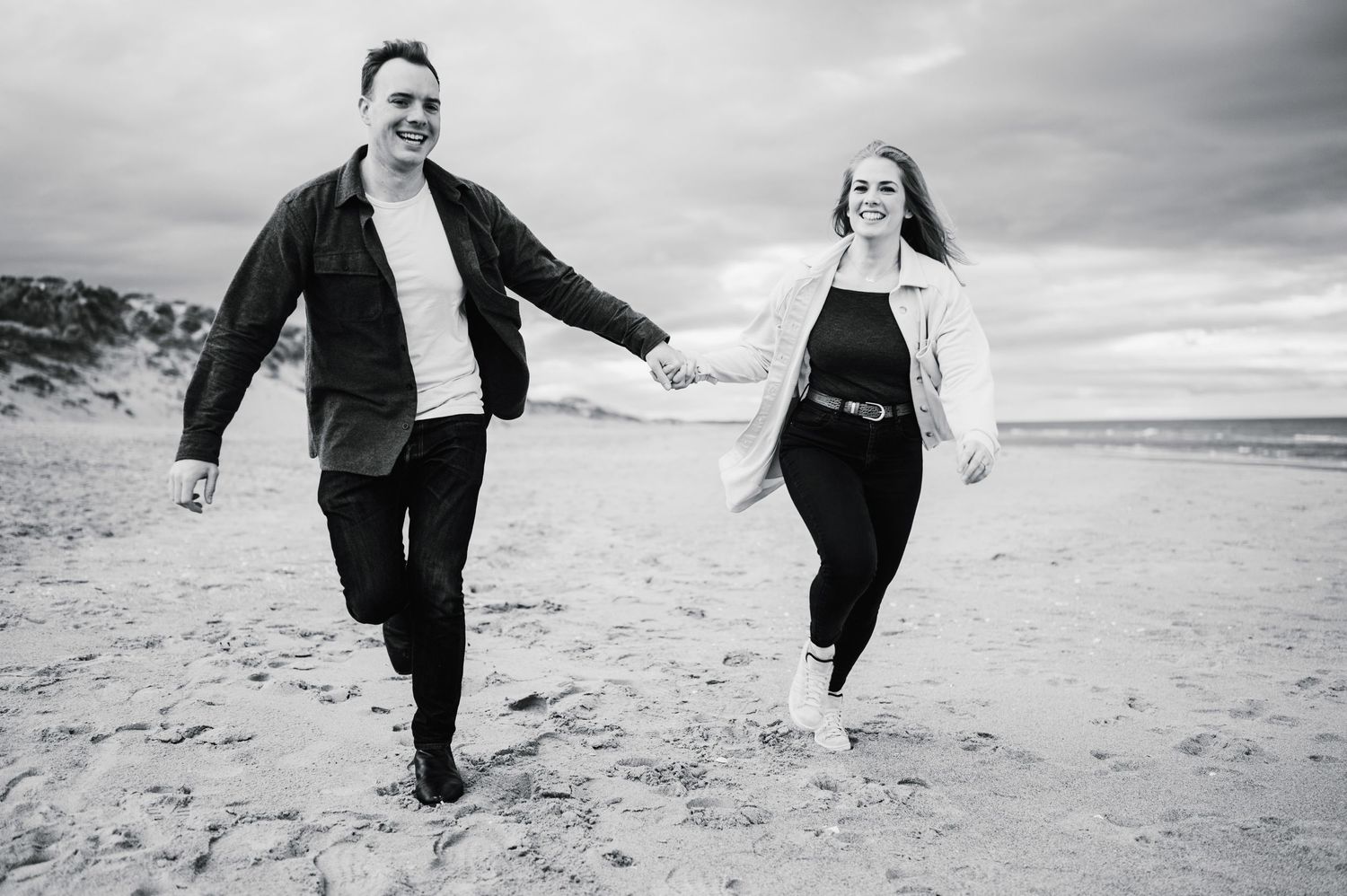 Couple takes a romantic stroll together on a sandy beach with cloudy skies.