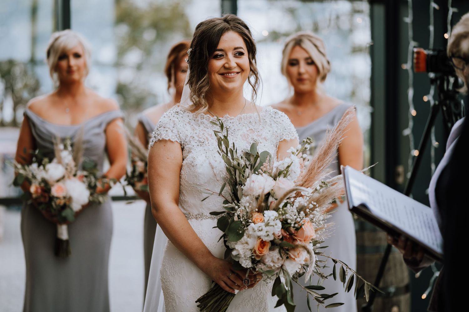 Bridesmaids in elegant gray dresses hold beautiful pastel bouquets at rustic venue.