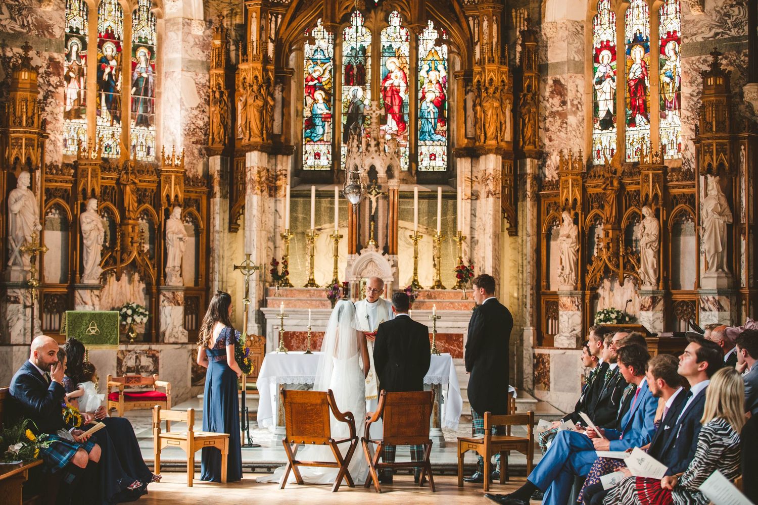 Wedding ceremony taking place in a historic church with elaborate stained glass windows and gothic details.