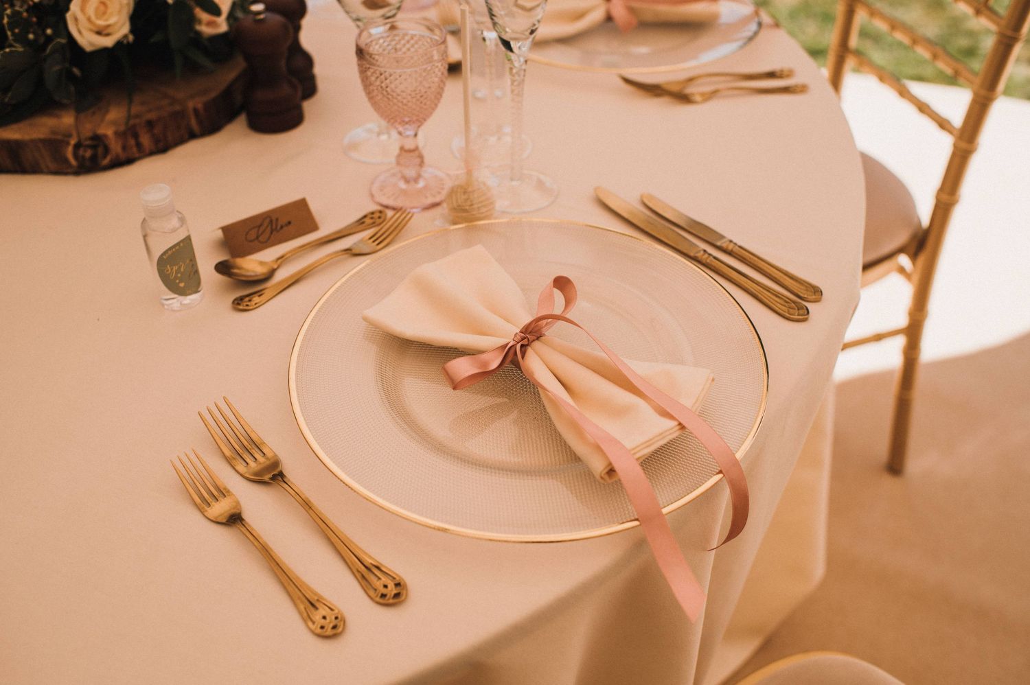 Elegant place setting with pink napkin, gold cutlery, and crystal glassware.