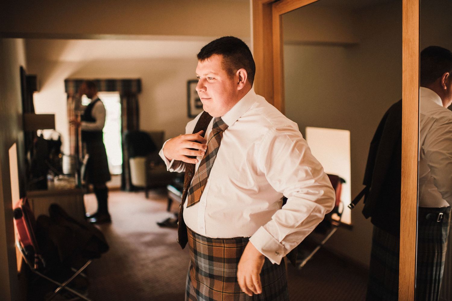 A person in traditional Scottish attire drinks from a bottle in a hotel room.