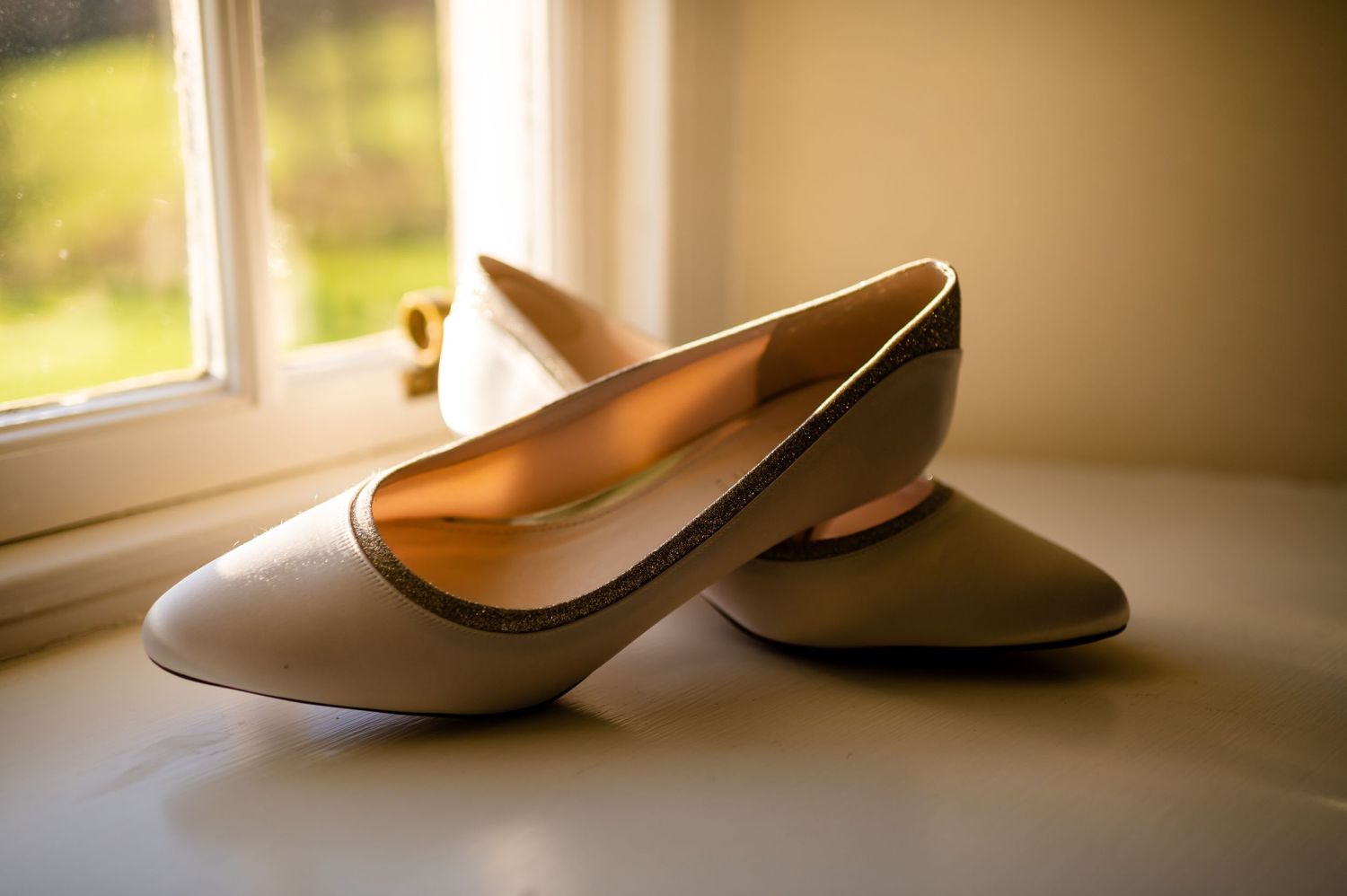 Pair of cream colored ballet flats sitting on a windowsill in natural light.