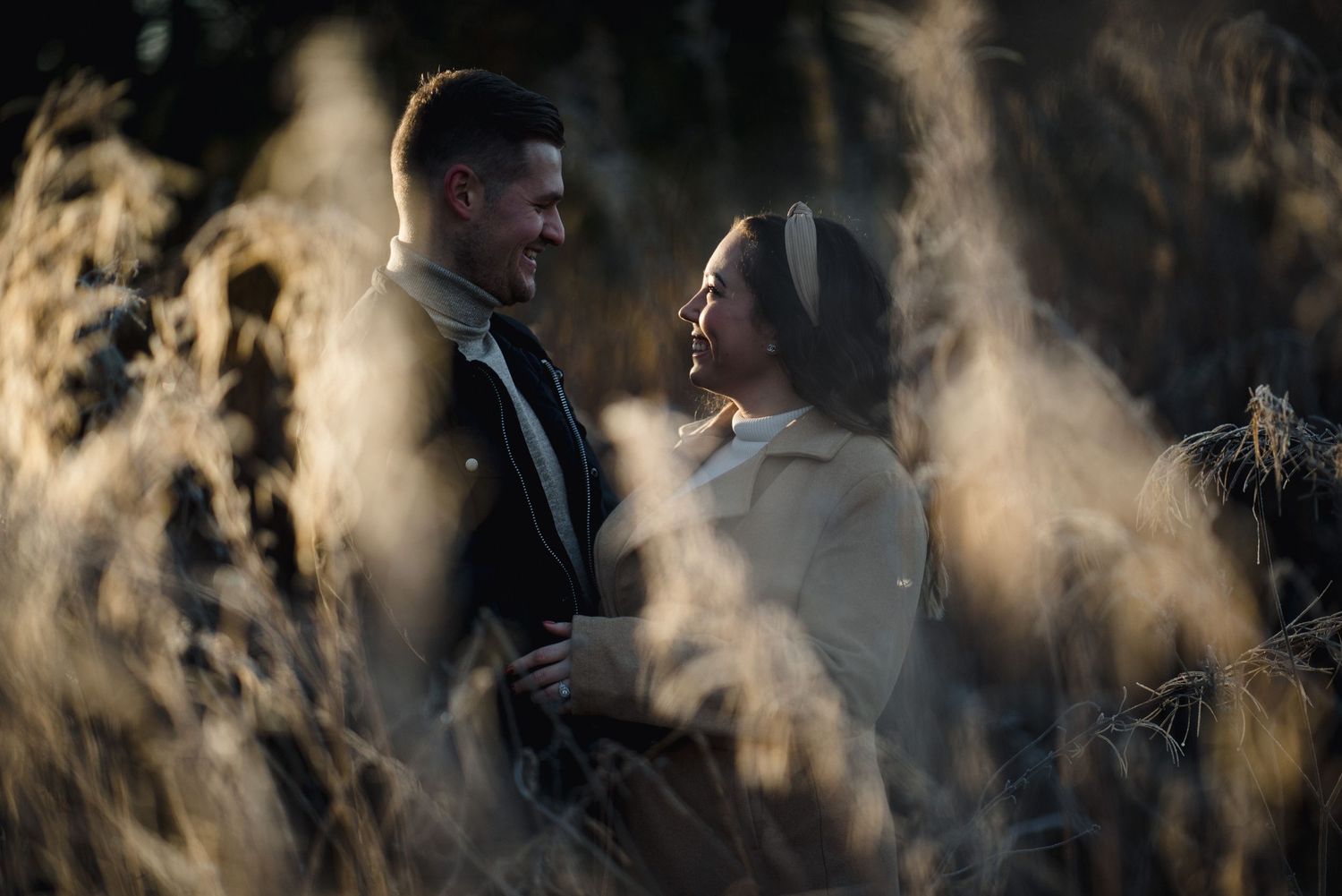A romantic winter engagement photo of a couple surrounded by misty backlit grasses at golden hour.