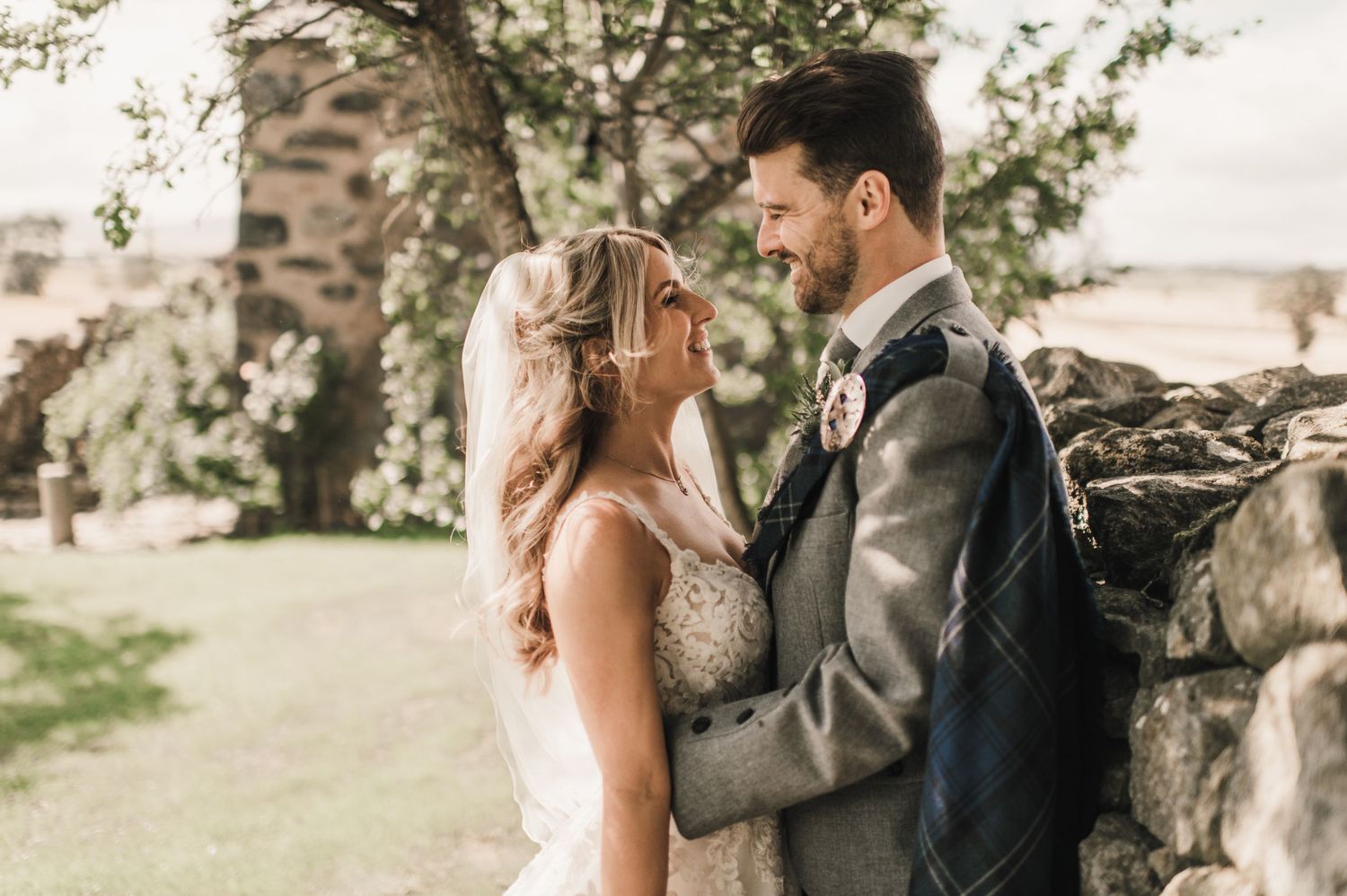 A tender moment between newlyweds against a rustic stone wall backdrop.