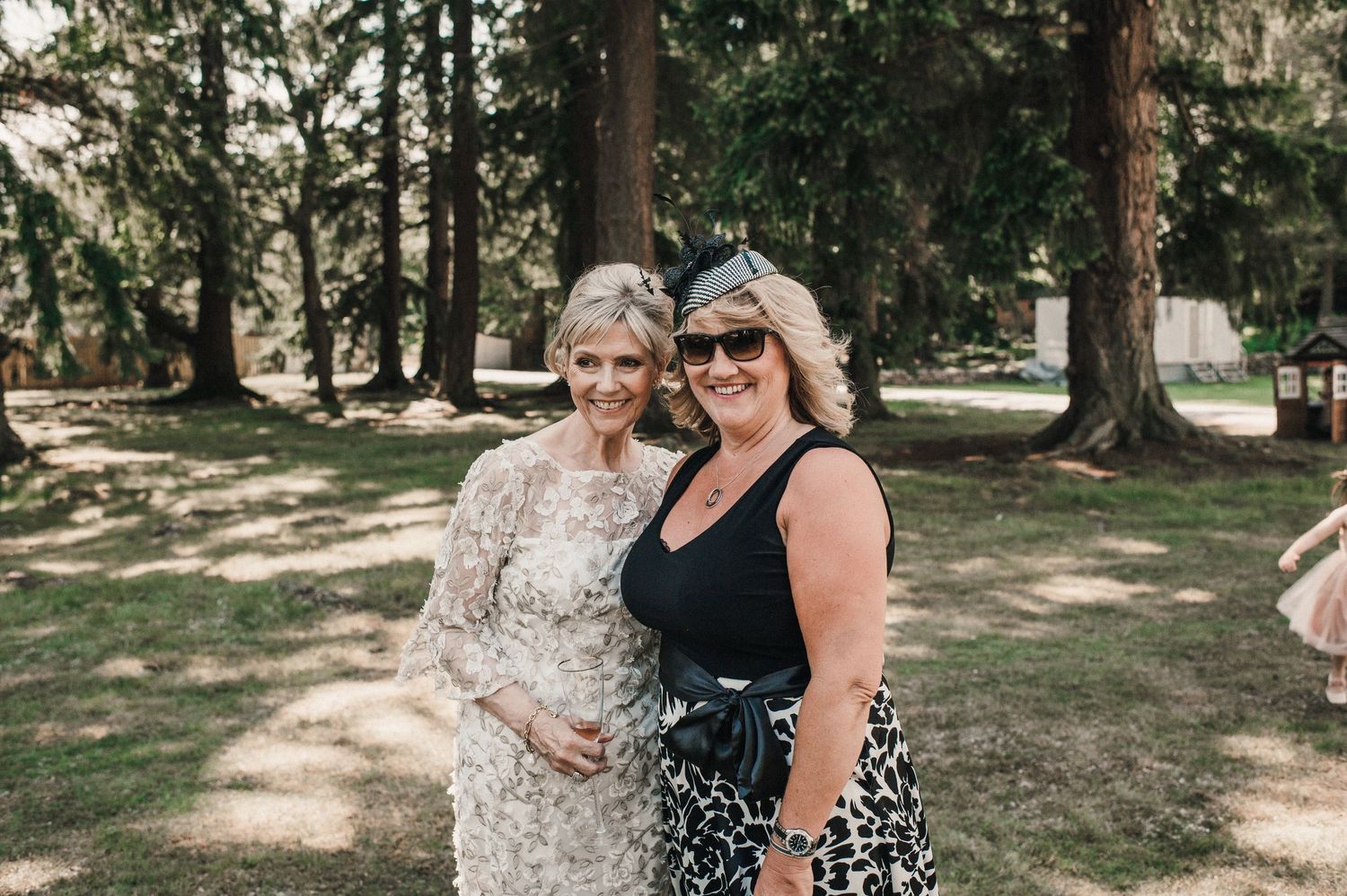 Two guests share a moment during an outdoor wedding celebration among tall trees.