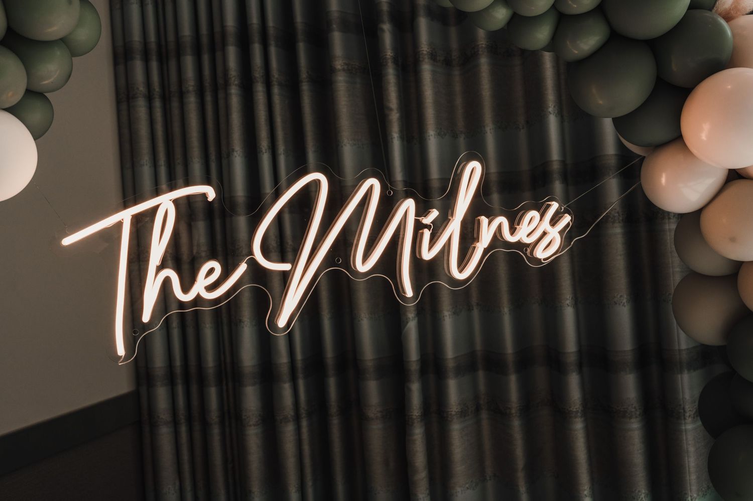 A neon sign reading 'The Milnes' glows against a backdrop of grey and white balloons.