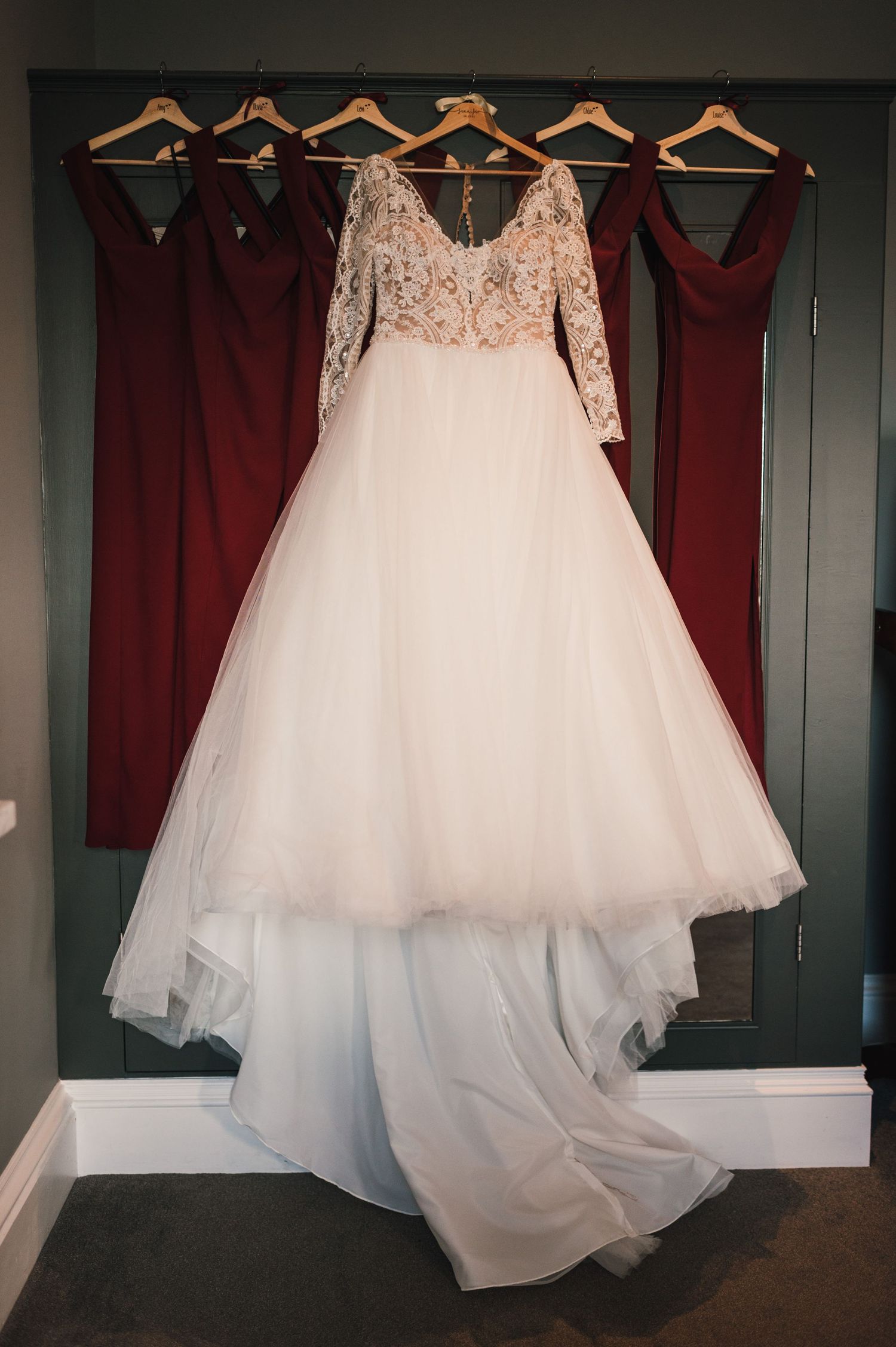 Wedding gown with lace top and tulle skirt hanging alongside burgundy bridesmaid dresses.