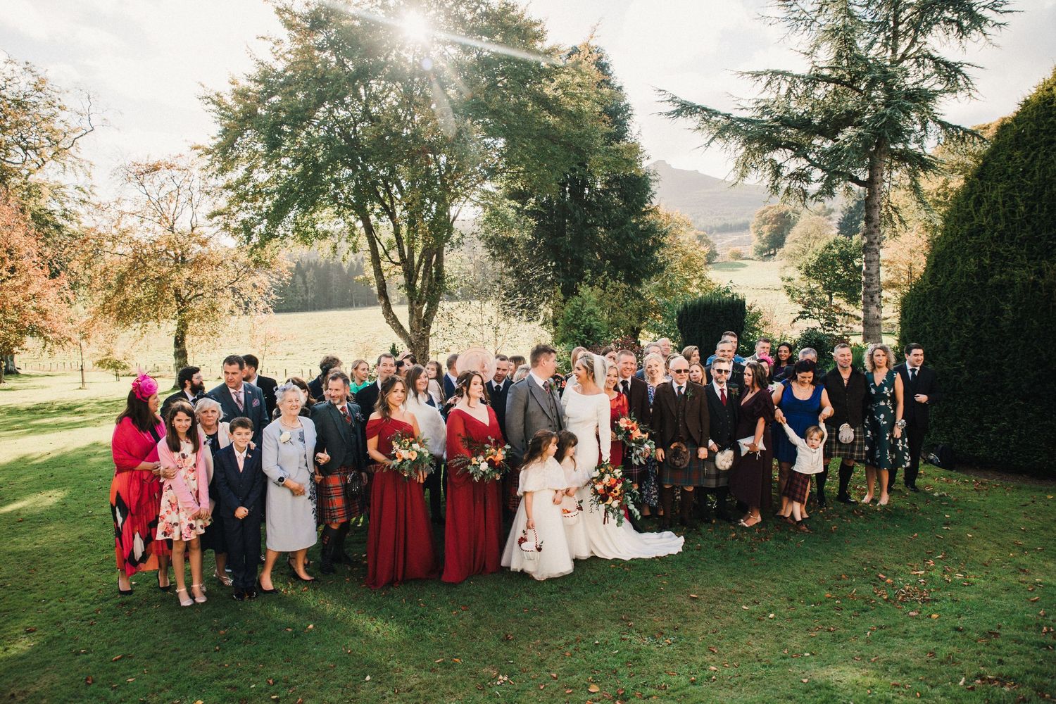 Large wedding party group photo on green lawn with Scottish kilts and burgundy dresses.