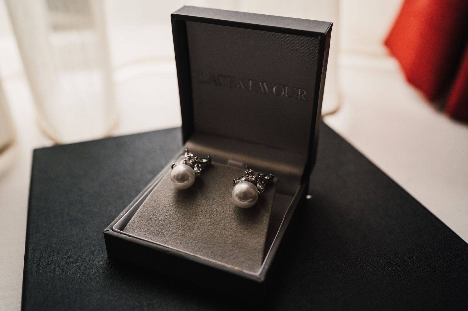 Black jewelry box containing elegant pearl cufflinks or earrings on dark surface.