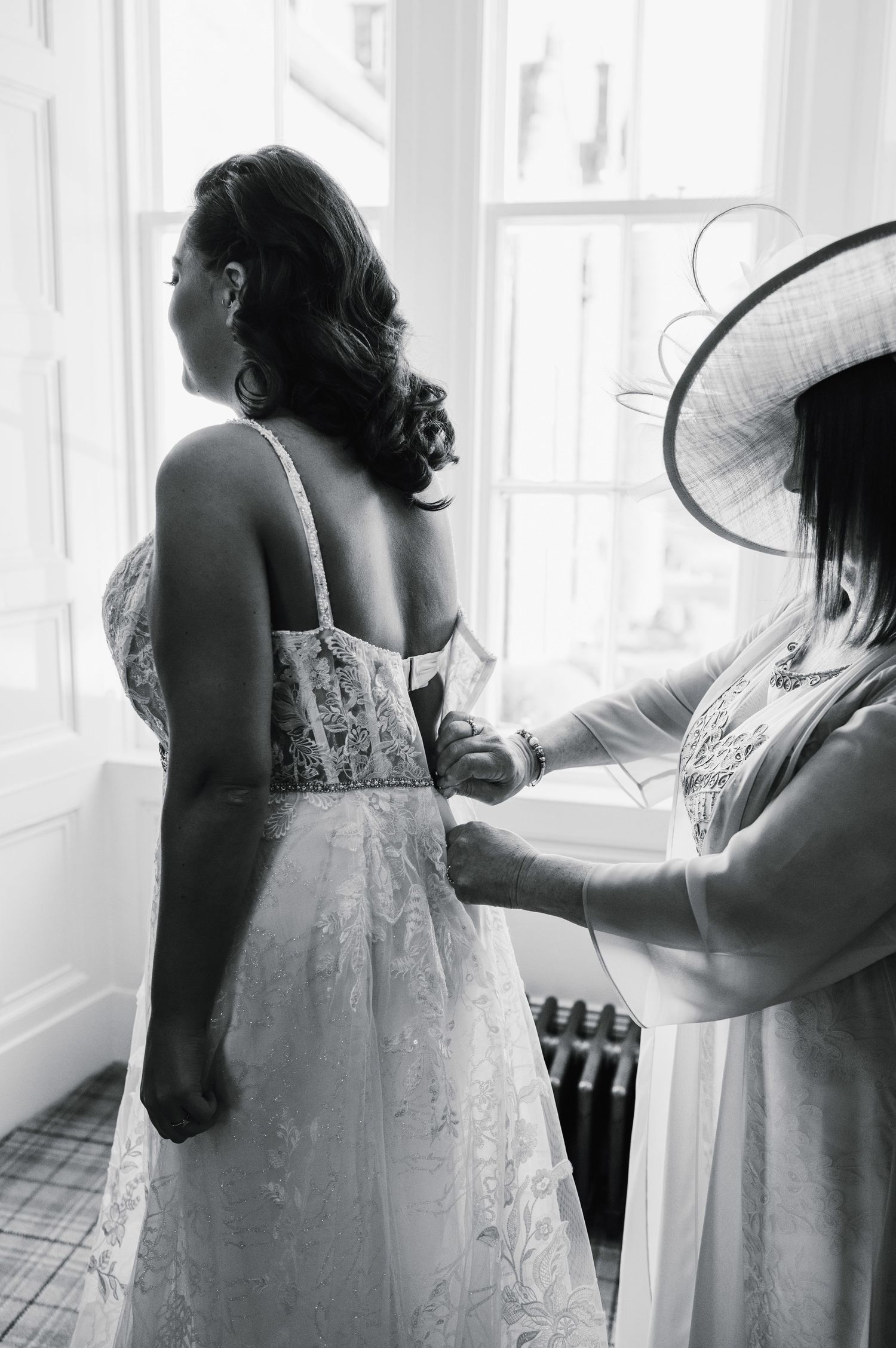A detailed lace wedding dress being adjusted in front of a bright window.