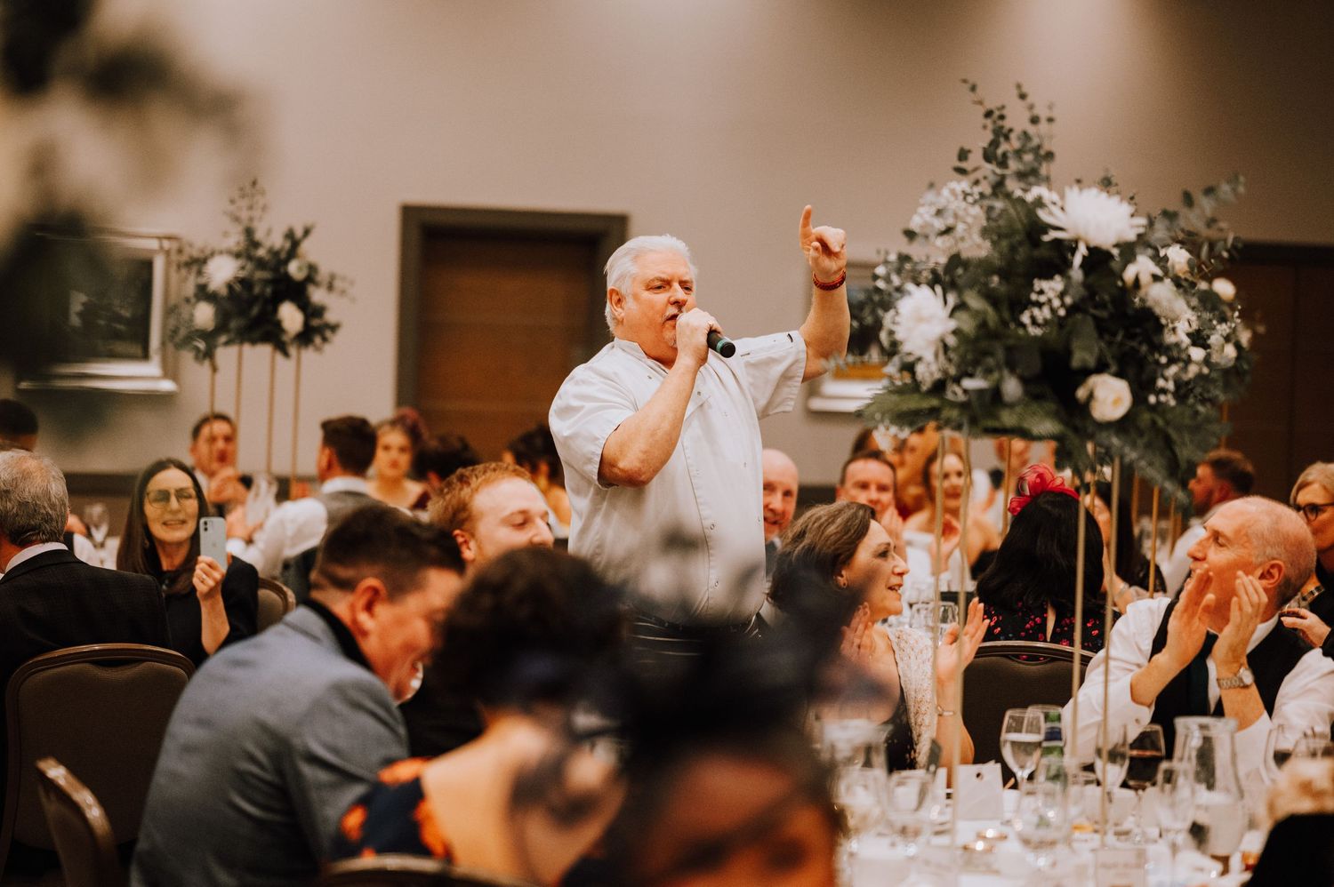 Wedding reception guests enjoying a lively celebration with floral decor and string lights in an elegant banquet room.