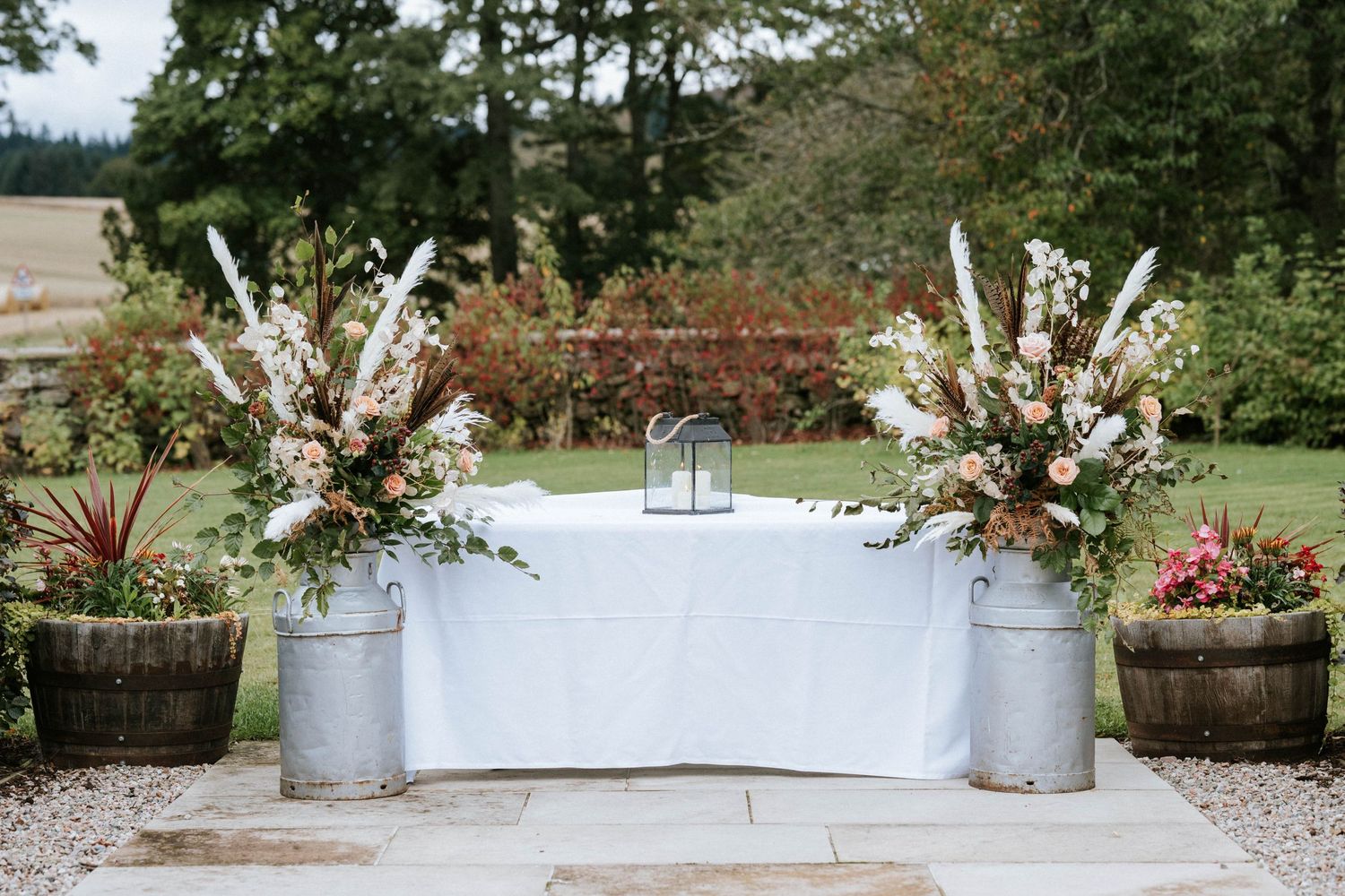 Outdoor wedding venue decorated with rustic metal planters and greenery along a stone pathway.