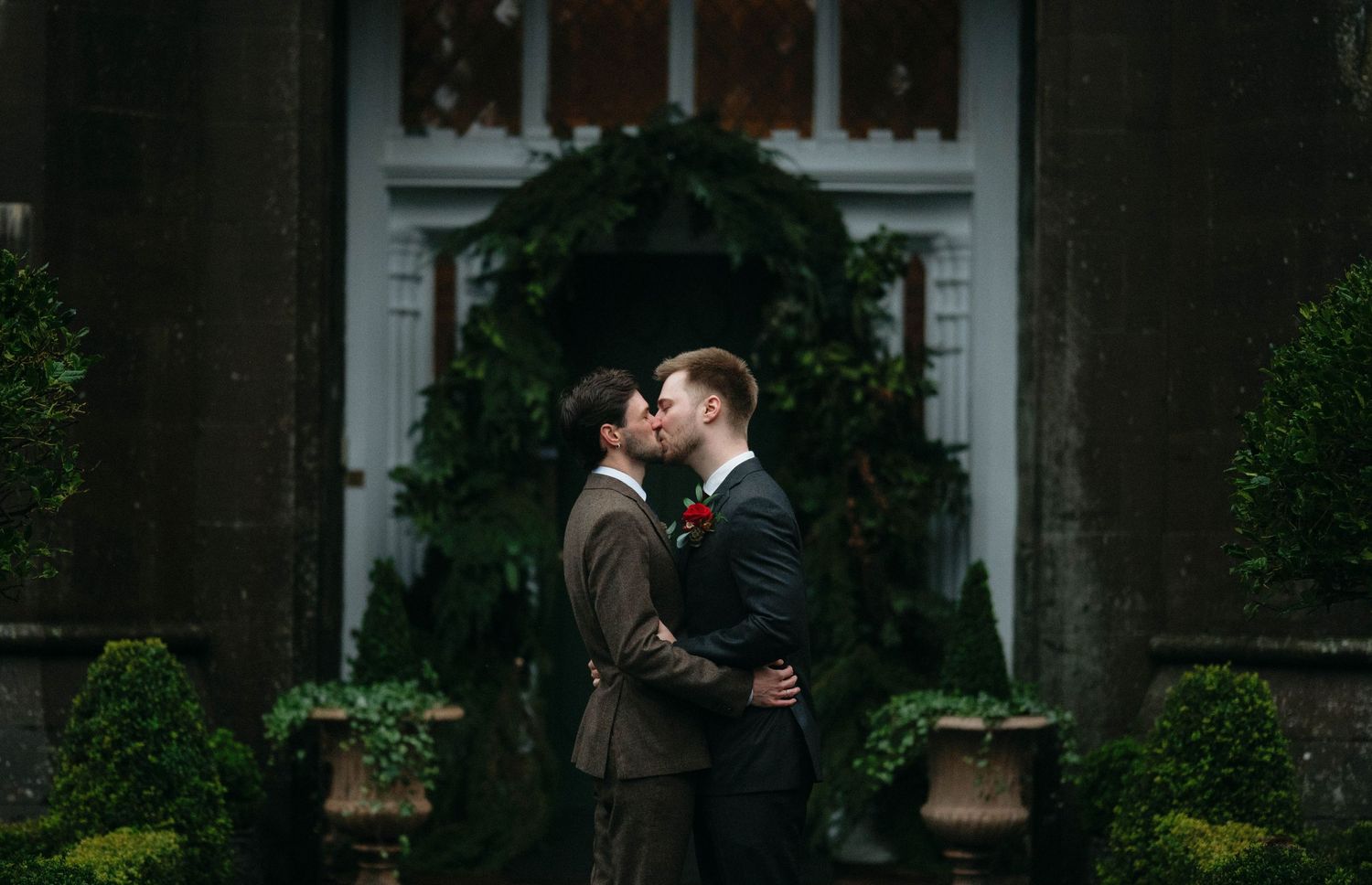 Wedding party stands in front of an elegant brick building with white trim and arched windows.
