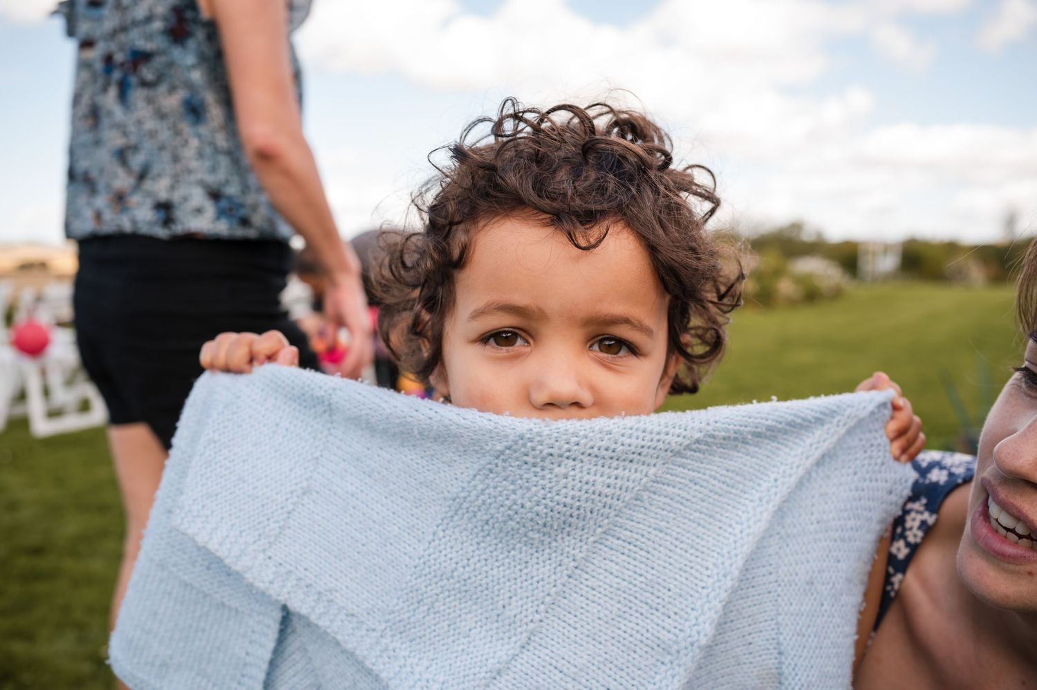 A joyful moment captured at an outdoor wedding ceremony with guests gathered on a grassy hillside.