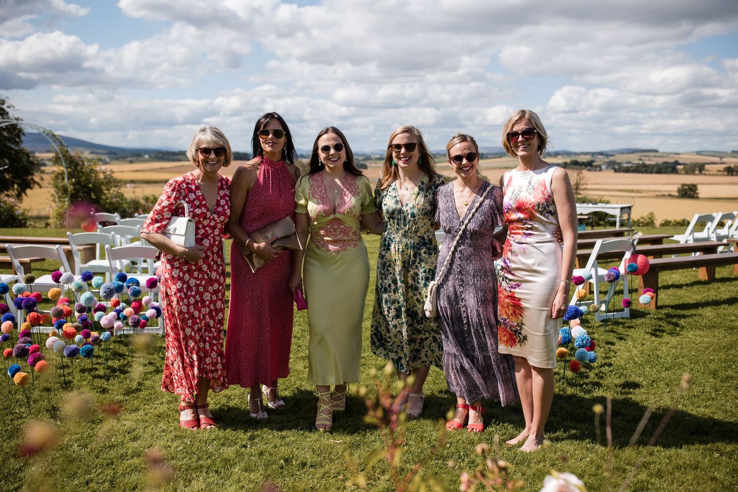 Wedding guests gathered outdoors on a grassy hill under cloudy skies.
