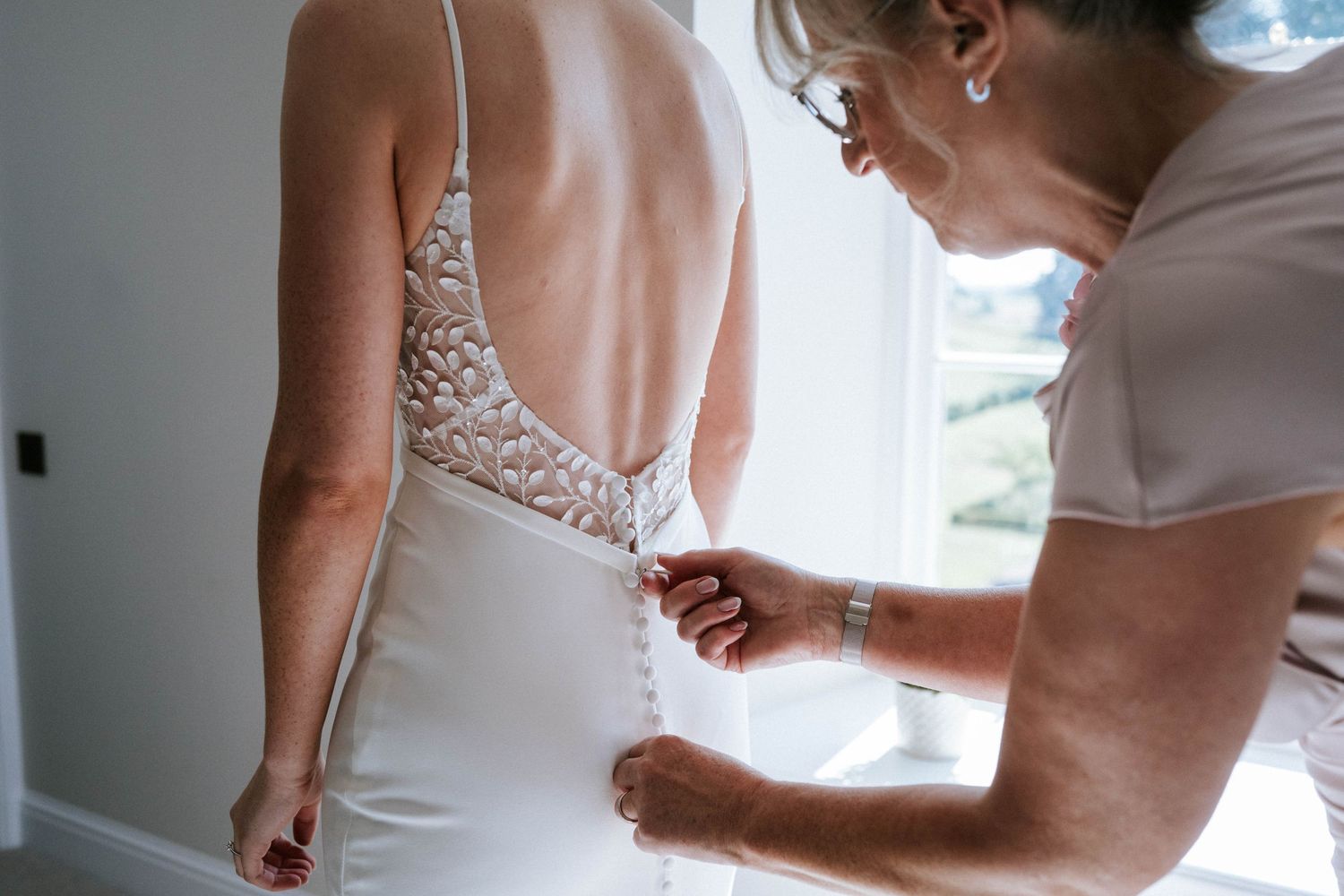 Close-up details of a bride getting dressed showing buttons and dress fastenings.