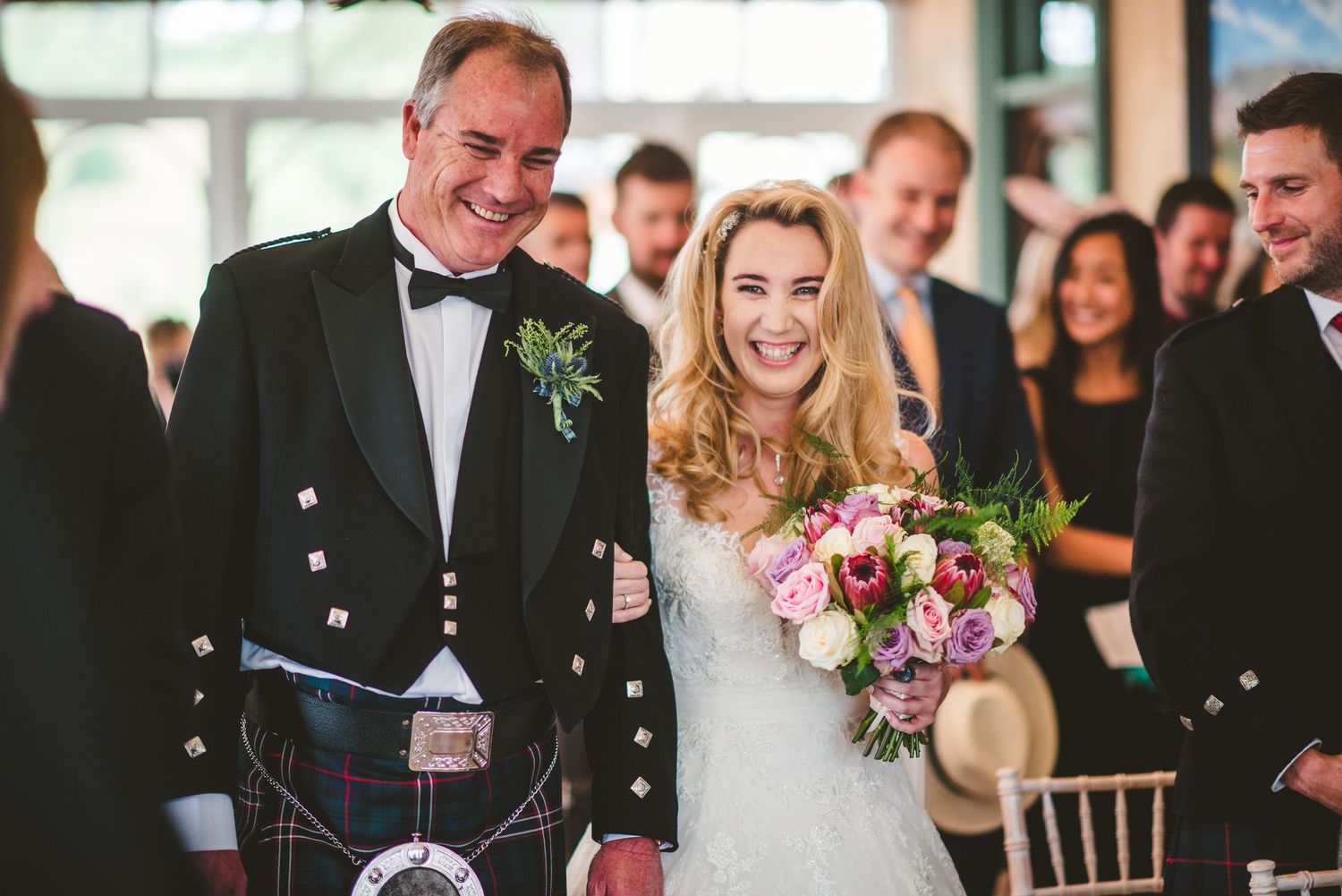 Wedding party celebrating in a traditional Scottish venue with kilts and formal attire.