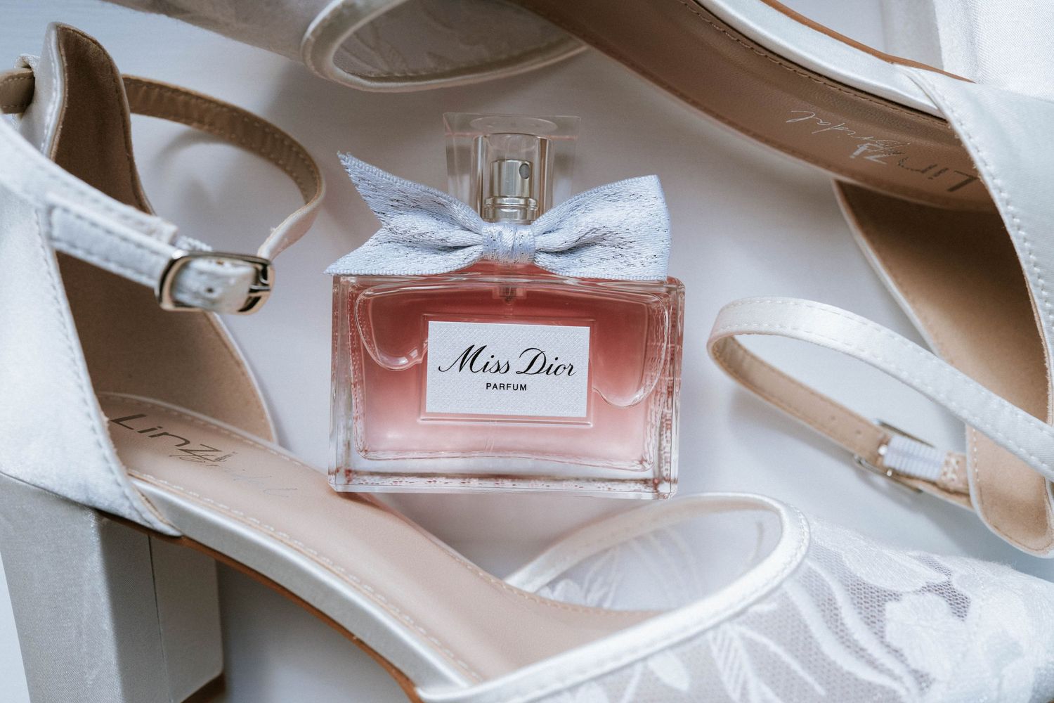Collection of Miss Dior perfume bottles and elegant high heel shoes arranged in soft lighting.
