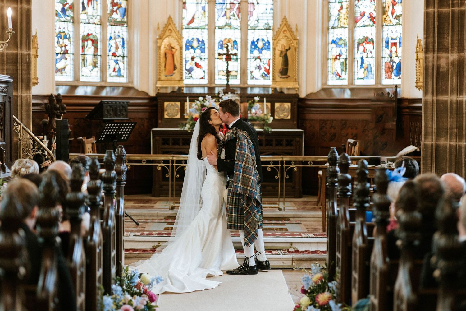 Traditional Scottish wedding ceremony in church with beautiful stained glass windows and floral decorations.