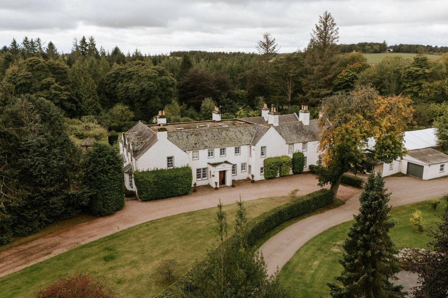 Aerial view of a Scottish countryside estate with white buildings and winding driveway surrounded by trees.