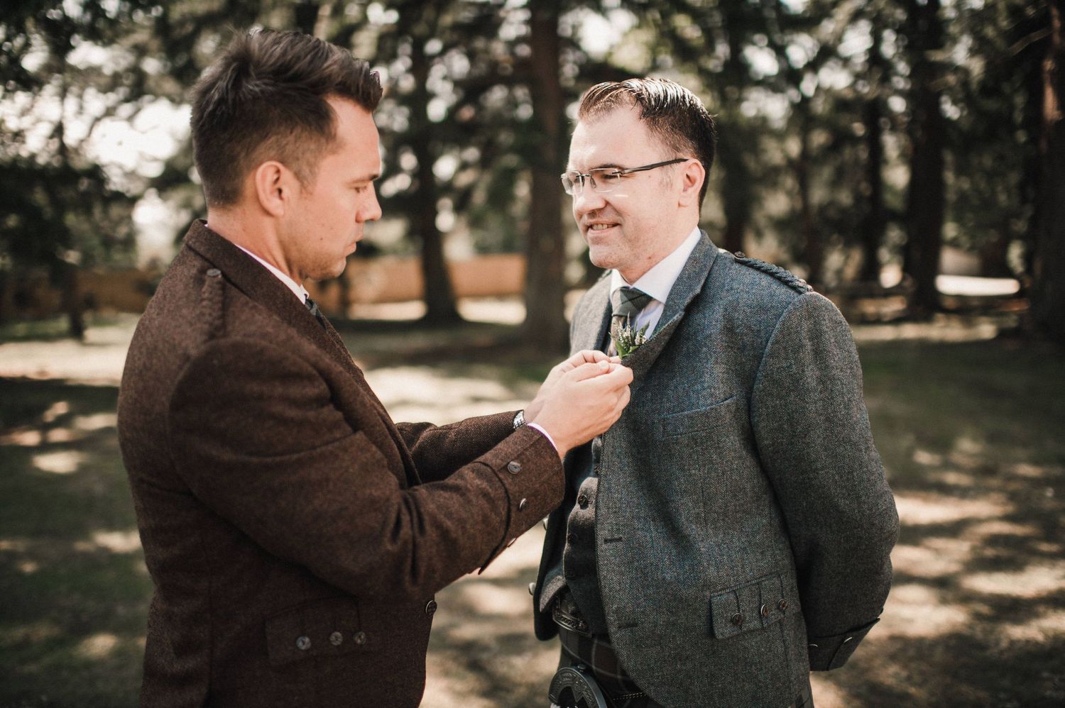 Two people sharing a candid moment while fixing formal attire outside.