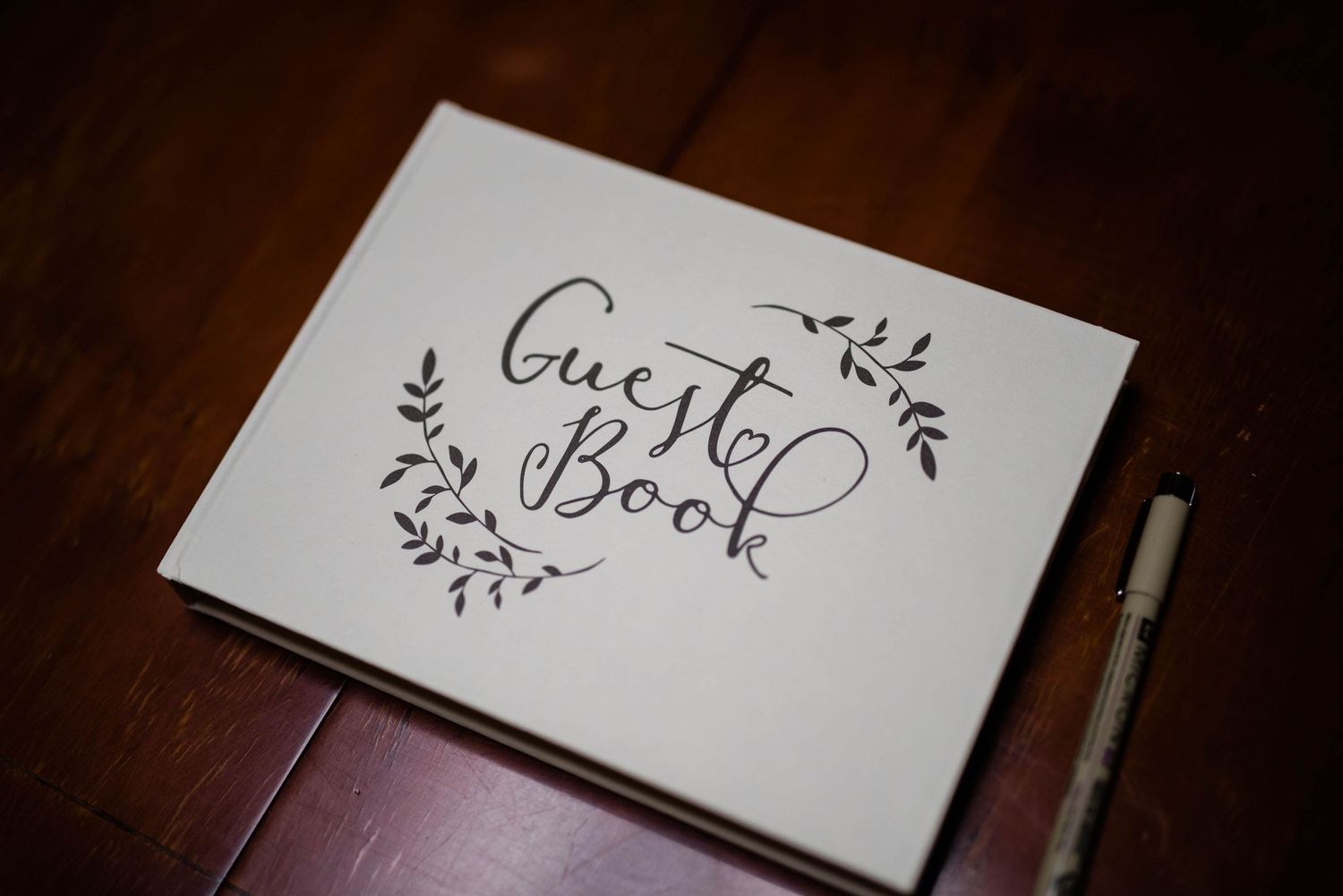 White wedding guest book with elegant calligraphy and floral design on dark wooden surface.