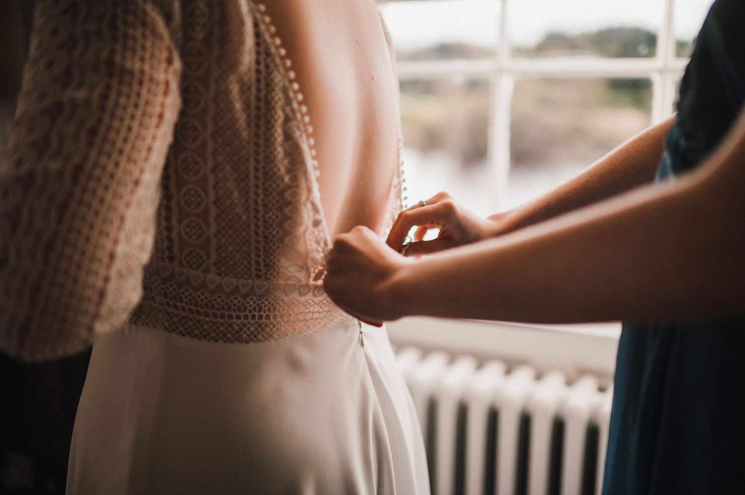 Close up detail of a white wedding dress being adjusted during bridal preparations.
