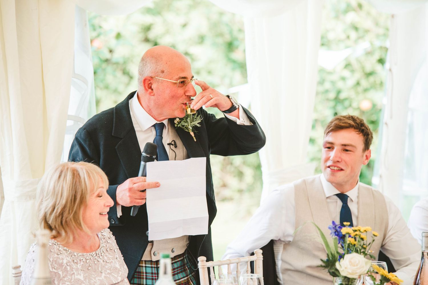 Emotional wedding speech moment during reception inside white marquee tent.