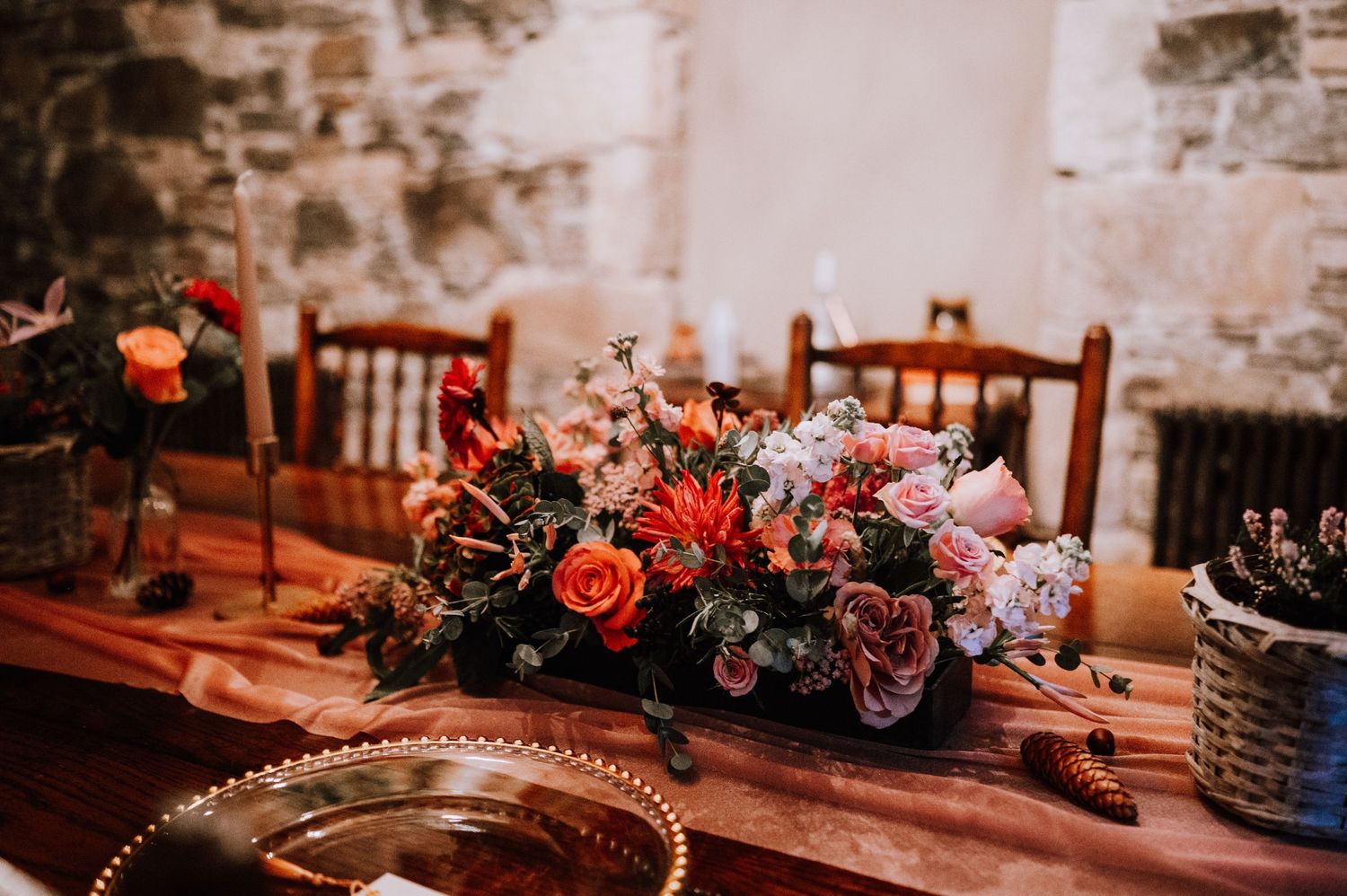 Elegant table setting with vibrant red and pink floral centerpiece in a rustic stone room.