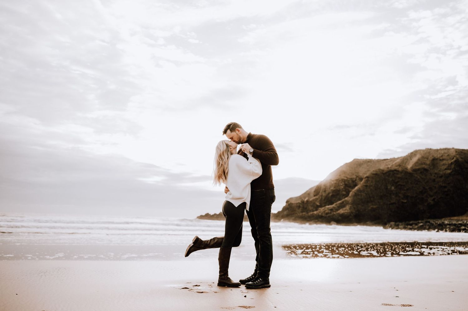 Romantic beach moment with couple embracing against coastal backdrop.