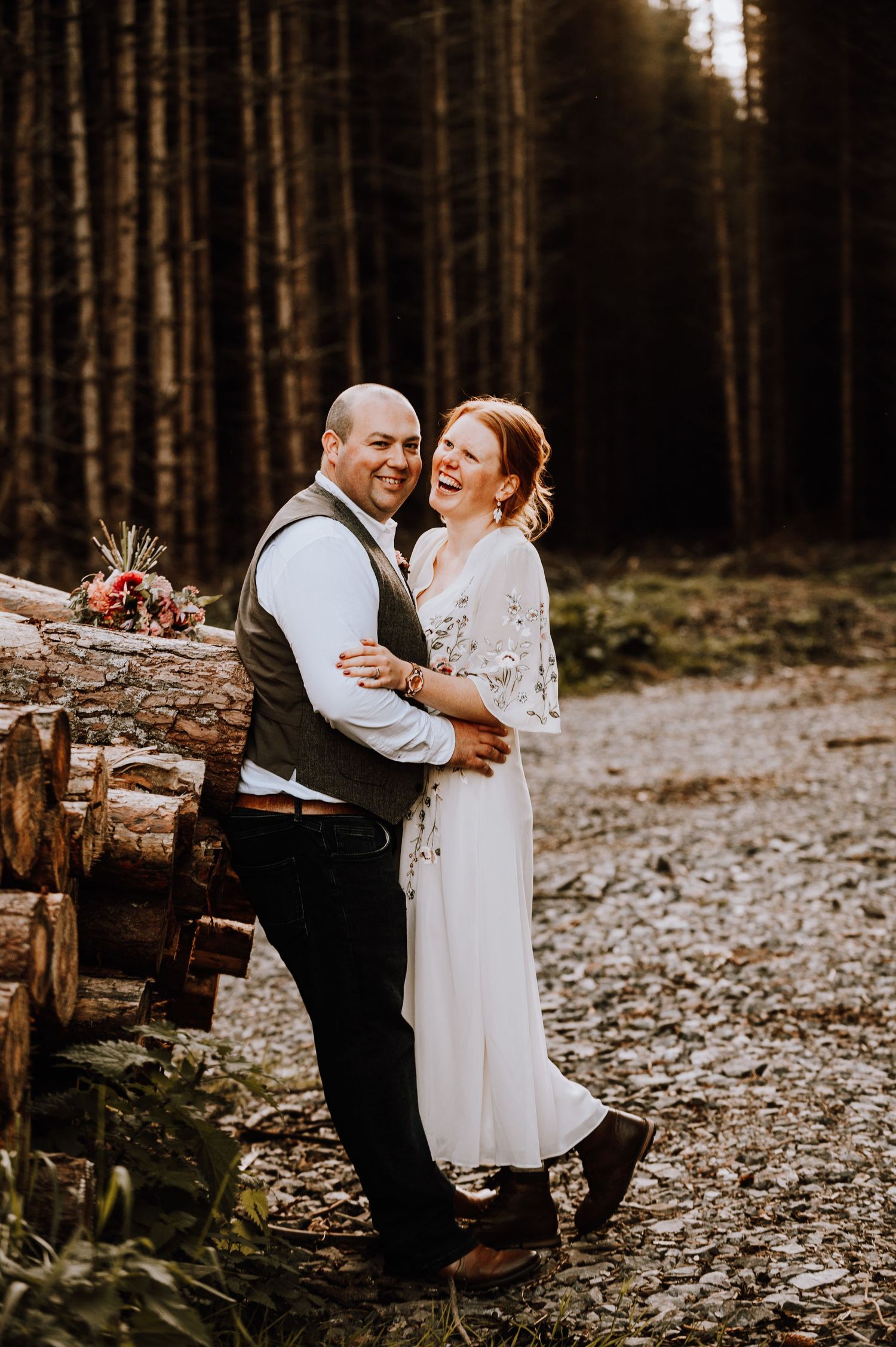 Rustic forest wedding portrait with couple embracing by stacked logs.