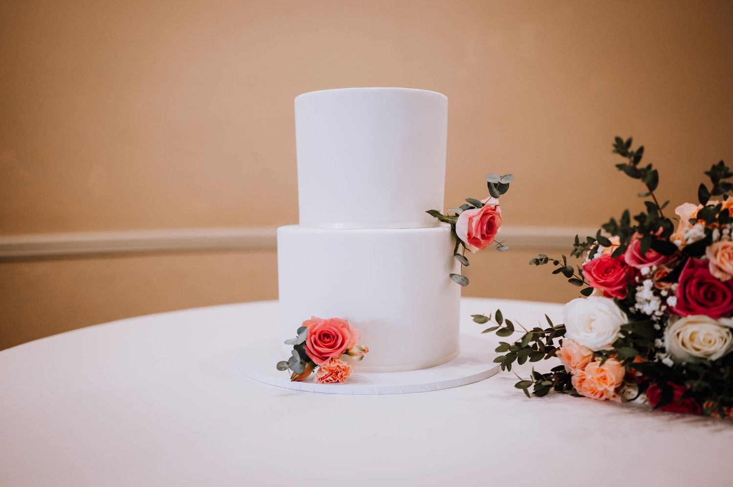 Simple white tiered wedding cake decorated with fresh coral roses.