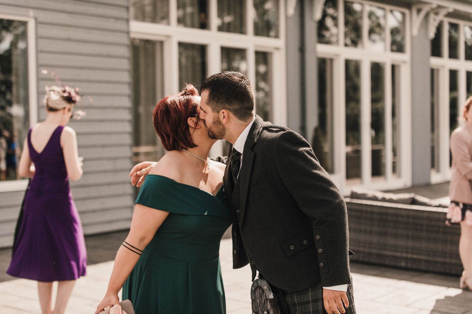 Couple sharing an intimate moment at an outdoor wedding venue with glass windows.